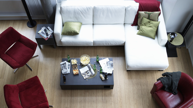 Top view of a white L-shaped sofa, red chairs, and an off-center black coffee table