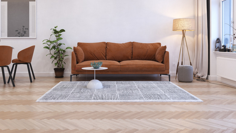 A living room with a herringbone floor, a brown sofa, and a patterned rug