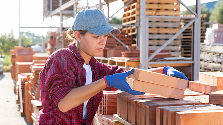 Woman picking up bricks from bricks stacked on pallet