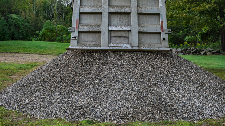 A dump truck unloads a pile of rock in a grassy yard.