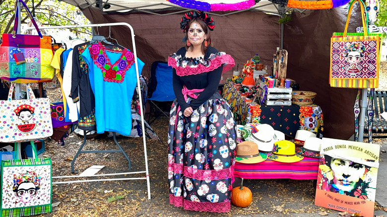 A woman wearing a Day of the Dead costume sells handmade items at a booth