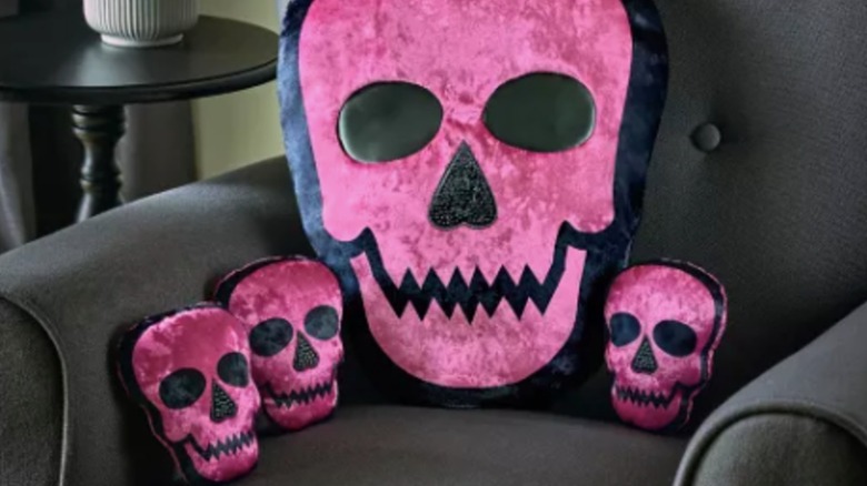 A large pink skull throw pillow and three small skull pillows sit on a gray chair