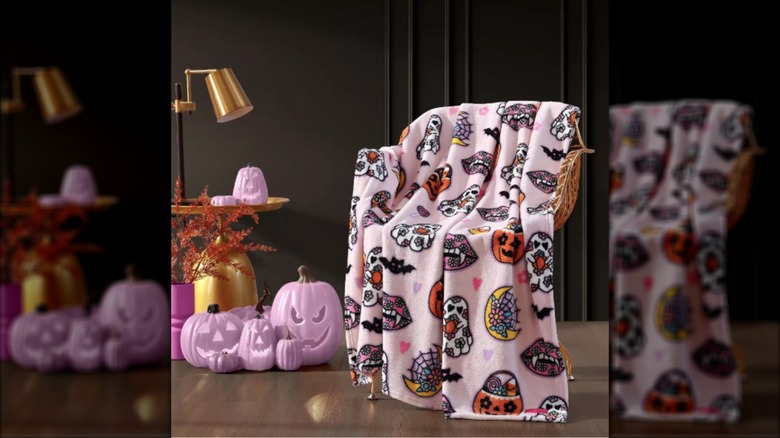 A pink Halloween-themed throw blanket is thrown over a chair surrounded by pink pumpkins.