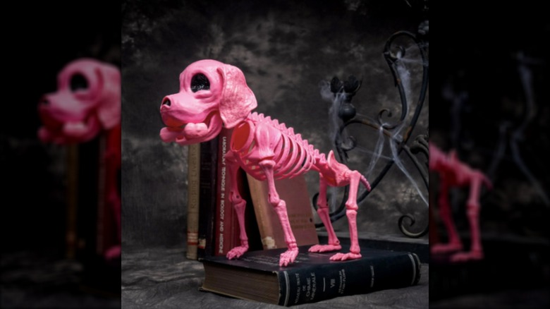 A plastic pink dog skeleton is posed amongst creepy Halloween decor