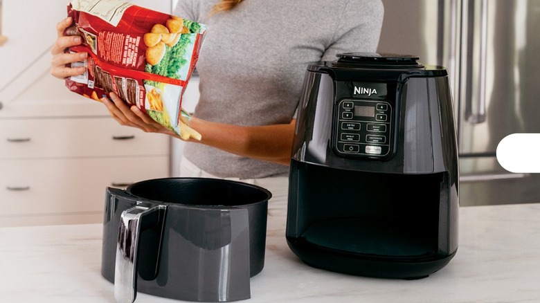 Woman adding frozen food into the basket of a black air fryer