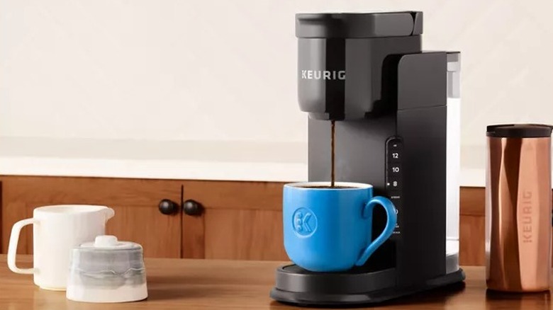 A black single serve Keurig pouring coffee into a blue mug