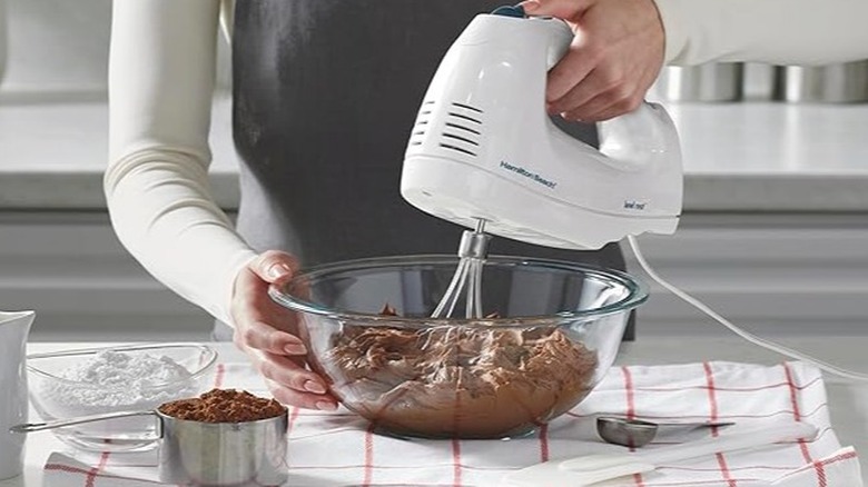 Woman using a white hand mixer to mix ingredients in a glass bowl