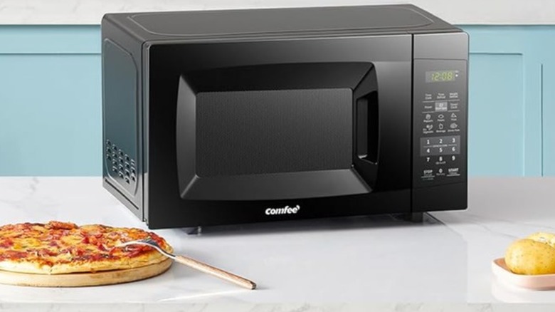 Black Comfee microwave on a countertop beside pizza