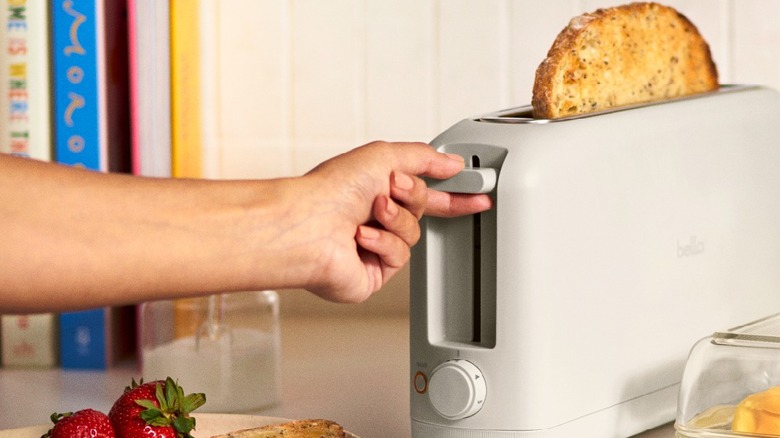 Hand using a lever on a slim gray toaster