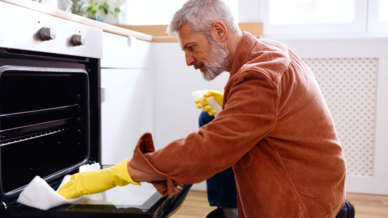 A man cleans the inside of the oven during spring cleaning in the kitchen