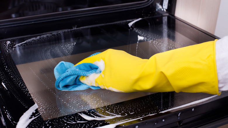 A gloved hand cleaning an oven door