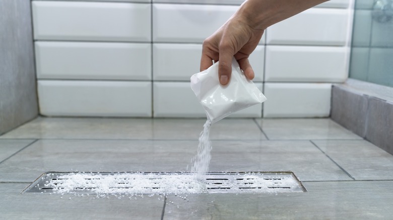 Hand pouring baking soda down shower drain