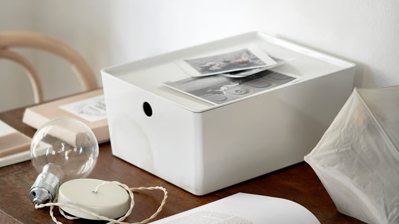 A white IKEA KUGGIS bins with a lid sitting on a cluttered table