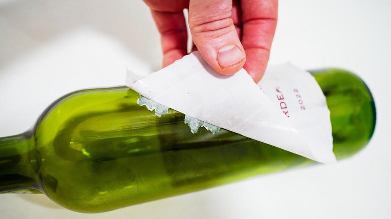 A person peels a sticker off a wine bottle.