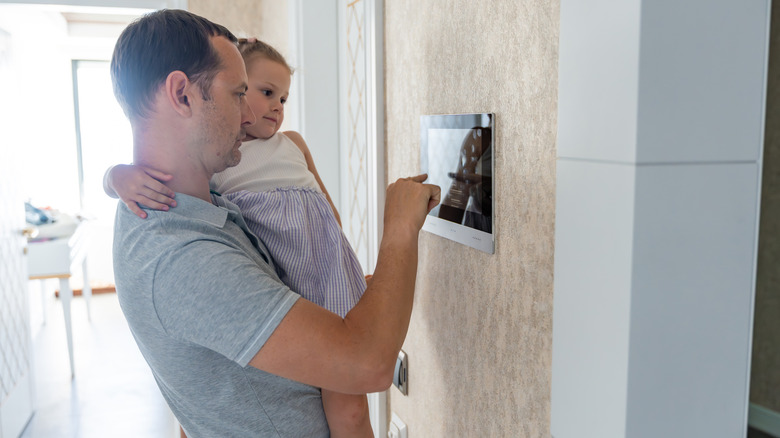 A dad sets his thermostat while holding daughter