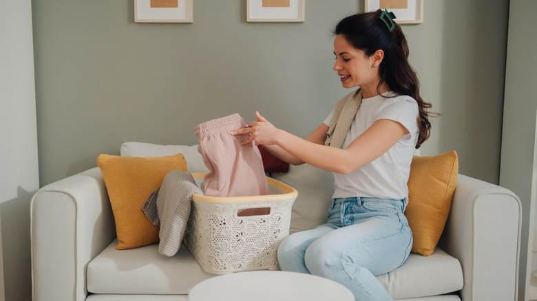 young woman sitting on sofa in living room folding and organizing clothes from a laundry basket