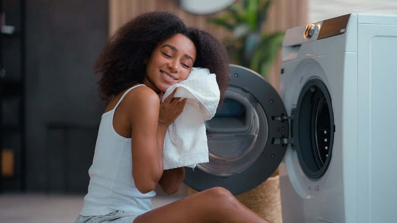 African American woman in front of open washing machine holding clean white towel to face