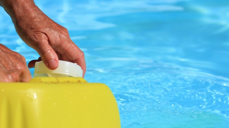 Hands open yellow chlorine container at pool
