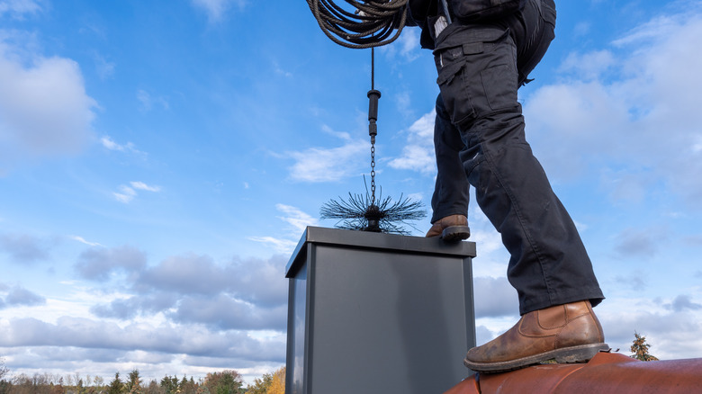 A chimney sweep on a roof cleaning a chimney