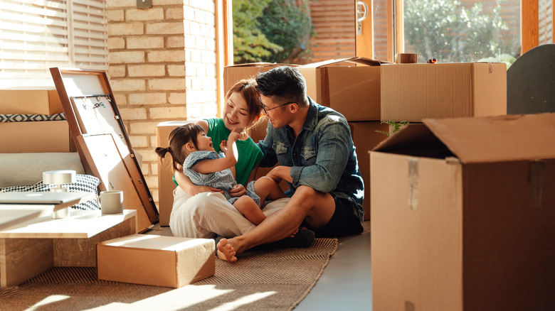 Young couple with daughter in their new home surrounded by moving boxes