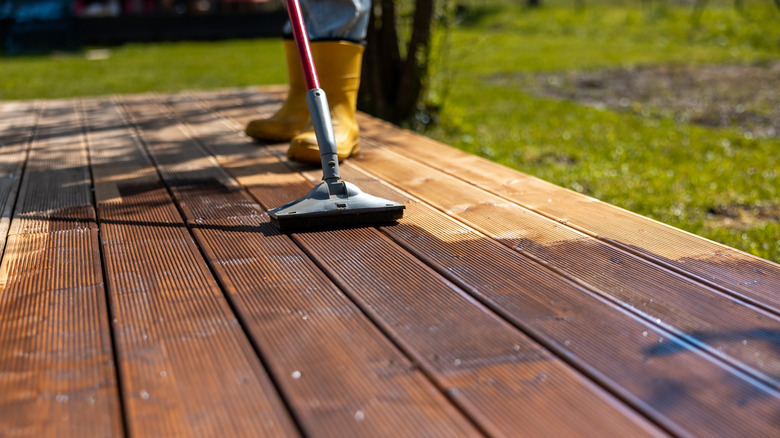 Person applying stain to a wooden deck in a backyard.