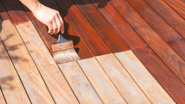 Person applying stain to a deck with a brush.