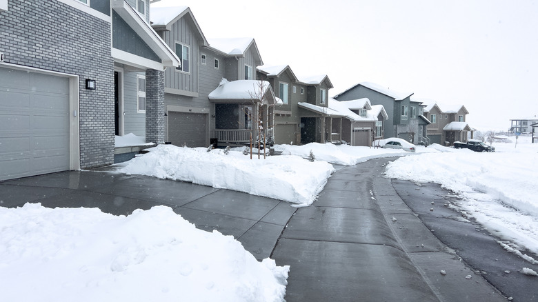 A residential neighborhood in winter with a walkway cleared for snow, bordered by snowbanks along the houses