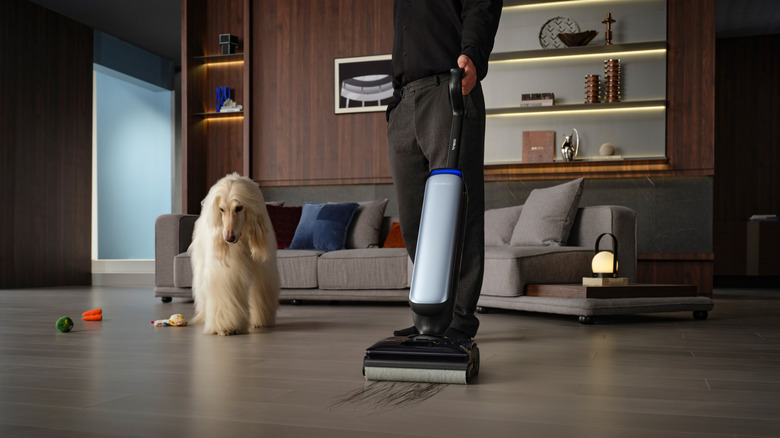 A dog watches a man using a Tineco vacuum mop to clean up hair off a hardwood floor