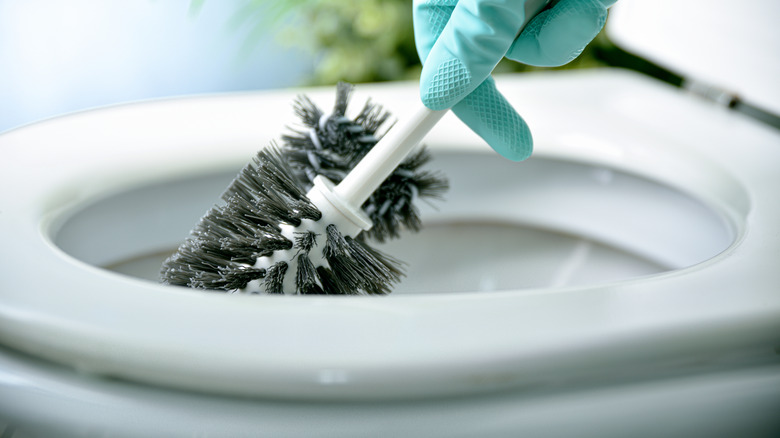 Gloved hand cleaning toilet with toilet bowl brush