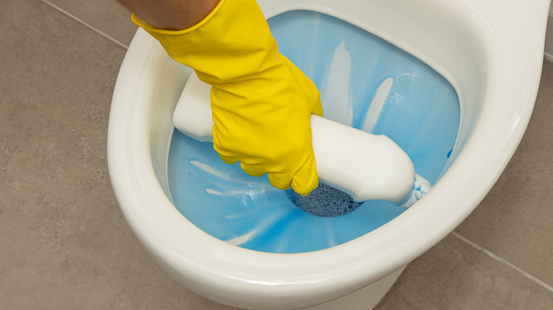 Gloved hand squirting toilet bowl cleaner in toilet bowl