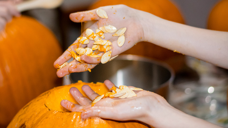 Person's hands covered in messy seeds from pumpkin