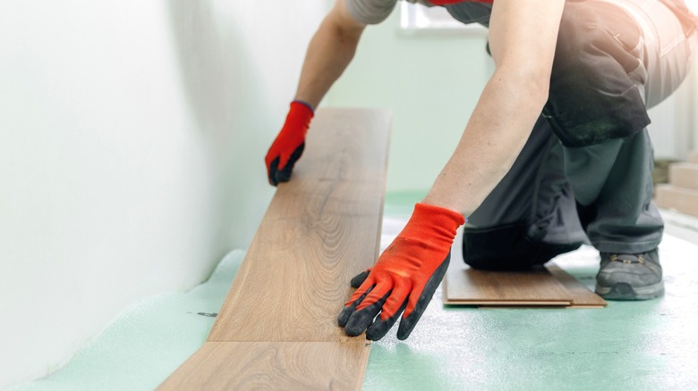man laying first line of laminate flooring on light green foam underlayment