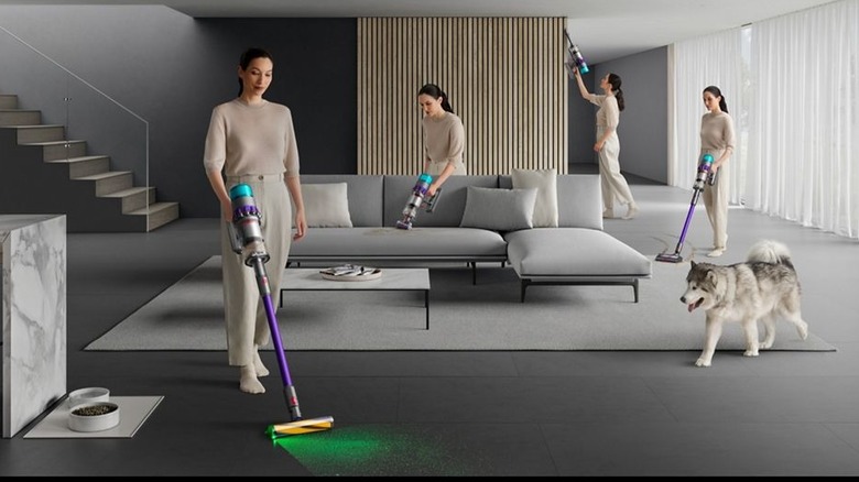 The Dyson Gen5 being used by the same woman in multiple areas of a room. A large husky dog is also walking across the floor.