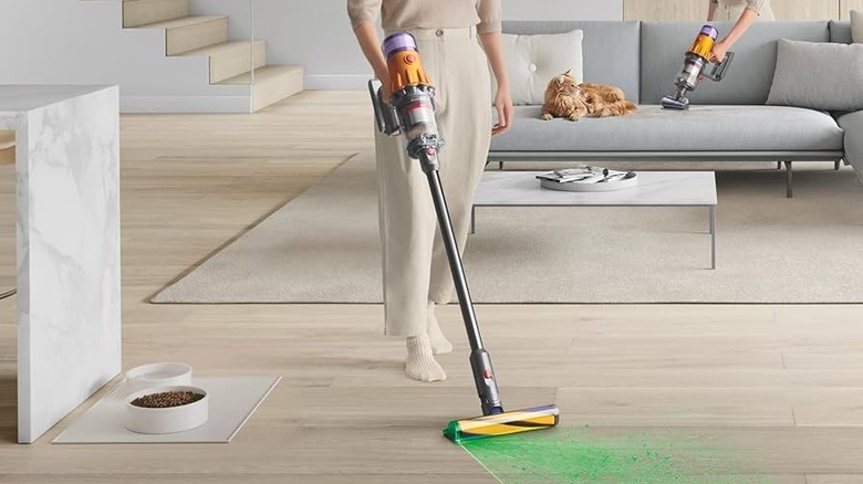 A woman vacuuming with the V12 showing its laser headlights. Behind her is a sofa with a long haired ginger cat and the same woman using the V12 as a handheld.