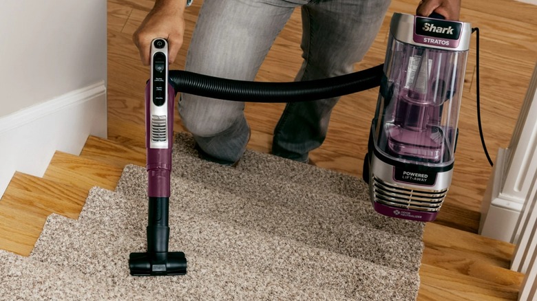 The Shark Stratos upright vacuuming on the edge of a rug and hard flooring with a woman's legs behind it.