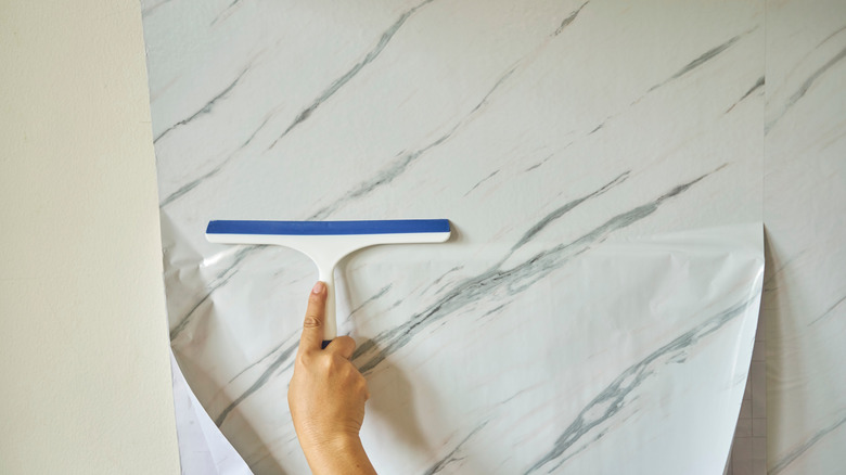 A person applies marbled wallpaper to a wall using a squeegee to remove air pockets
