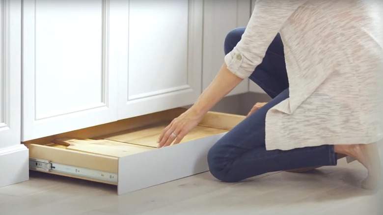 Woman taking cutting board from open toe-kick drawer in kitchen