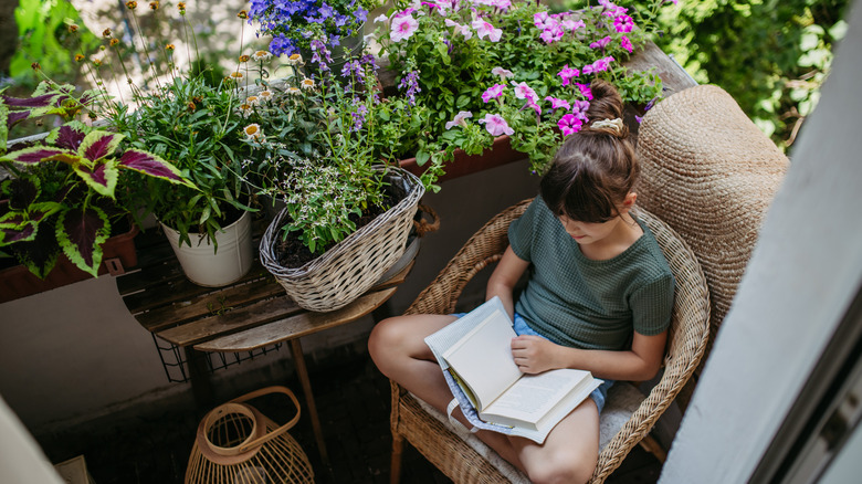 Woman sitting on a chair reading a book next to a balcony garden