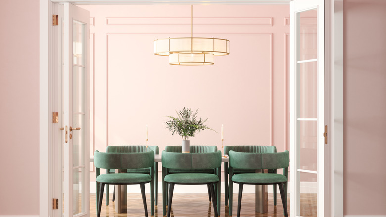 A glass chandelier above a dining table with green velvet chairs
