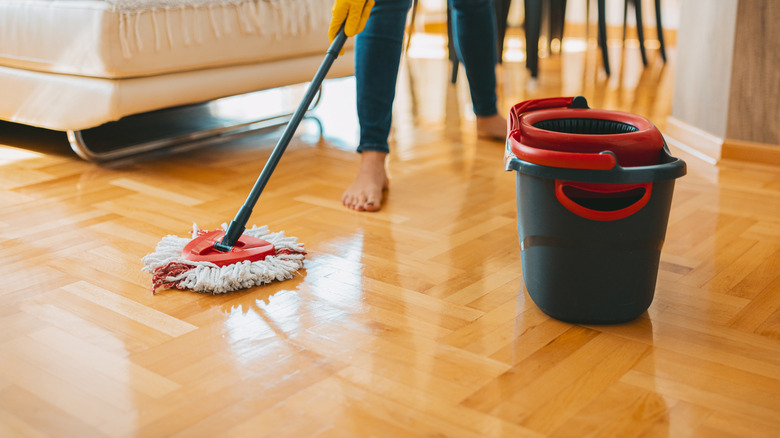 Close-up of a person cleaning parquet with a mop and a bucket