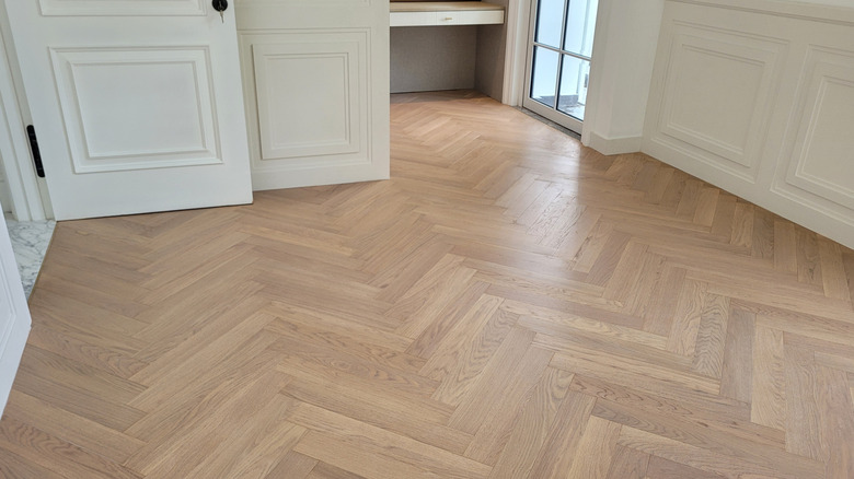 An empty room with white walls and doors and herringbone wood flooring
