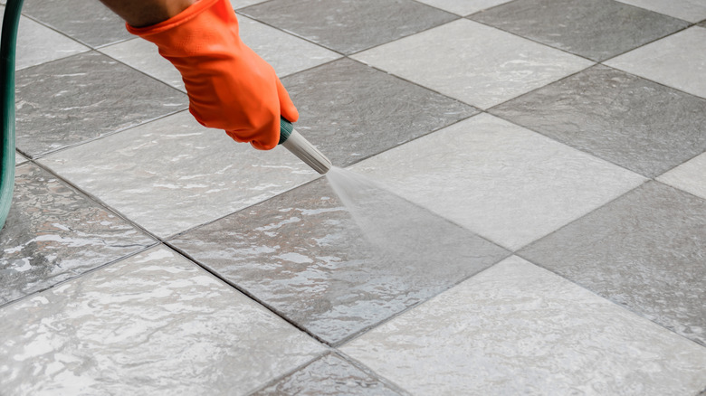 Person rinsing pavers with garden hose