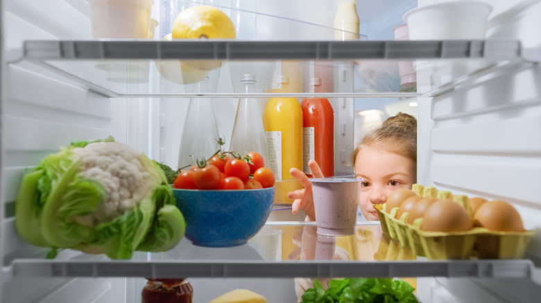 Girl retrieves food from refrigerator