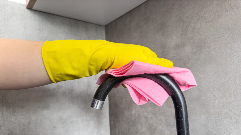 Yellow gloved hand wiping a clean faucet dry with a pink cloth