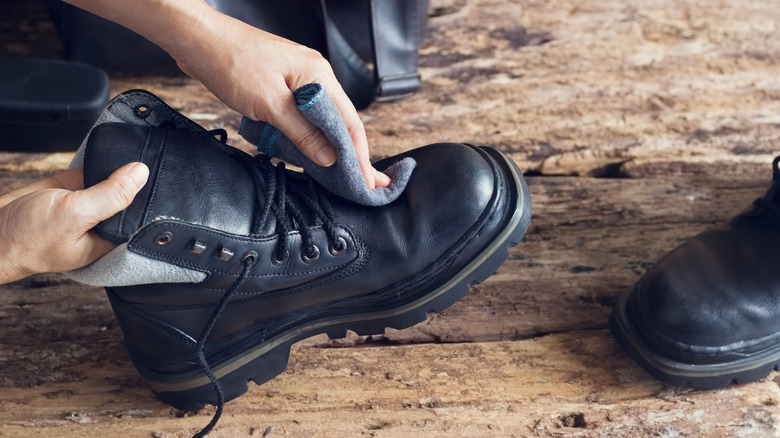 Person using blue cloth to clean a pair of black boots.
