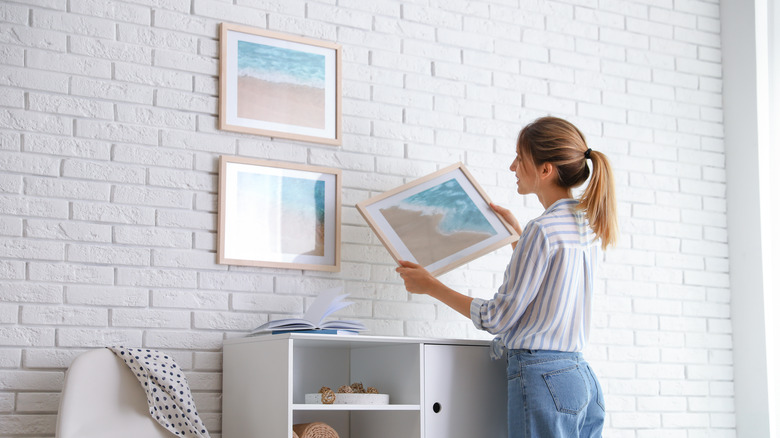 Person hanging pictures brick wall