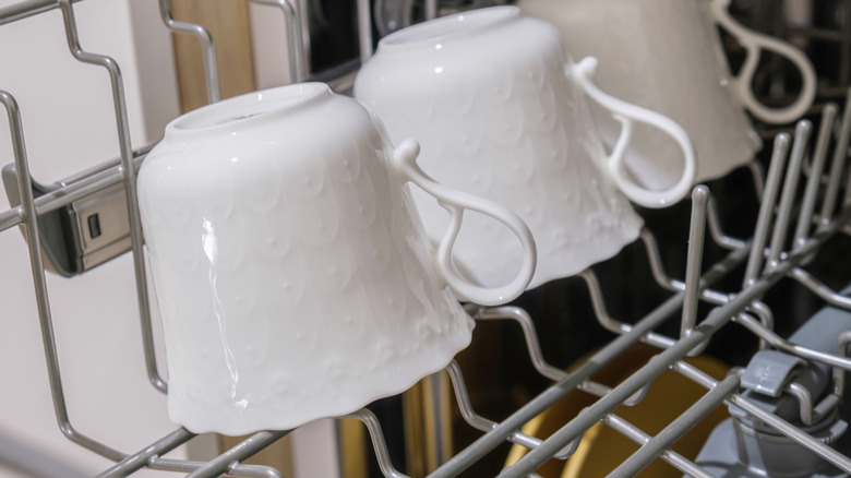 Three teacups placed at an angle on the top rack of a dishwasher