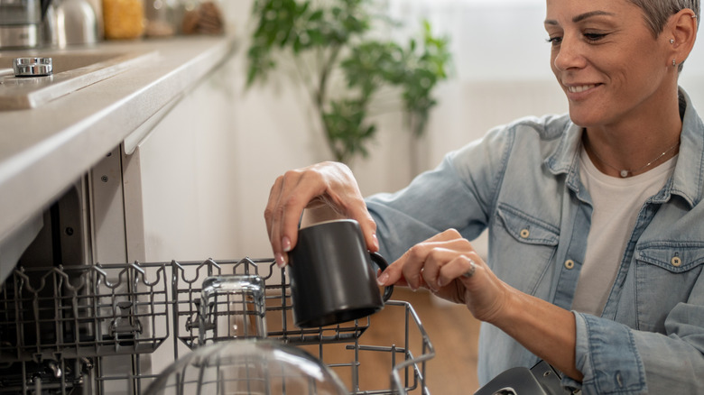 A person places a mug in a dishwasher