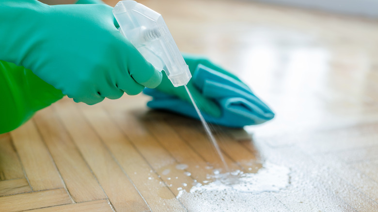 Hand spraying product on wood floor and holding a cleaning cloth