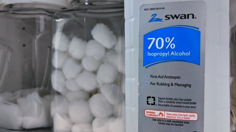 Isopropyl alcohol and a container of cotton balls in a medical cabinet.